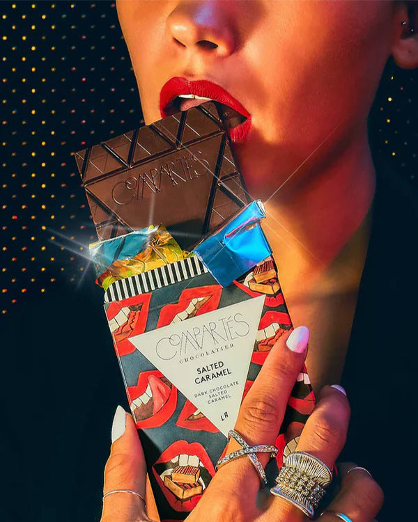 A mouth with red lips biting into a Compartes salted caramel chocolate bar.