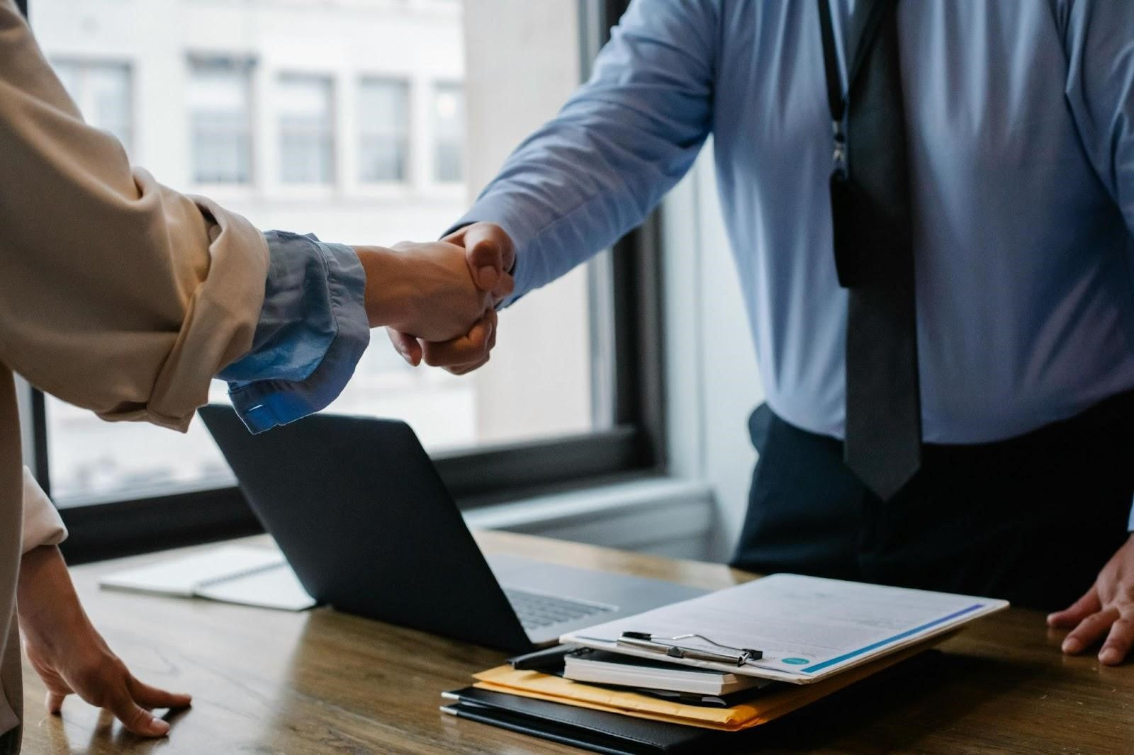 Two colleagues exchange a handshake in a corporate setting.