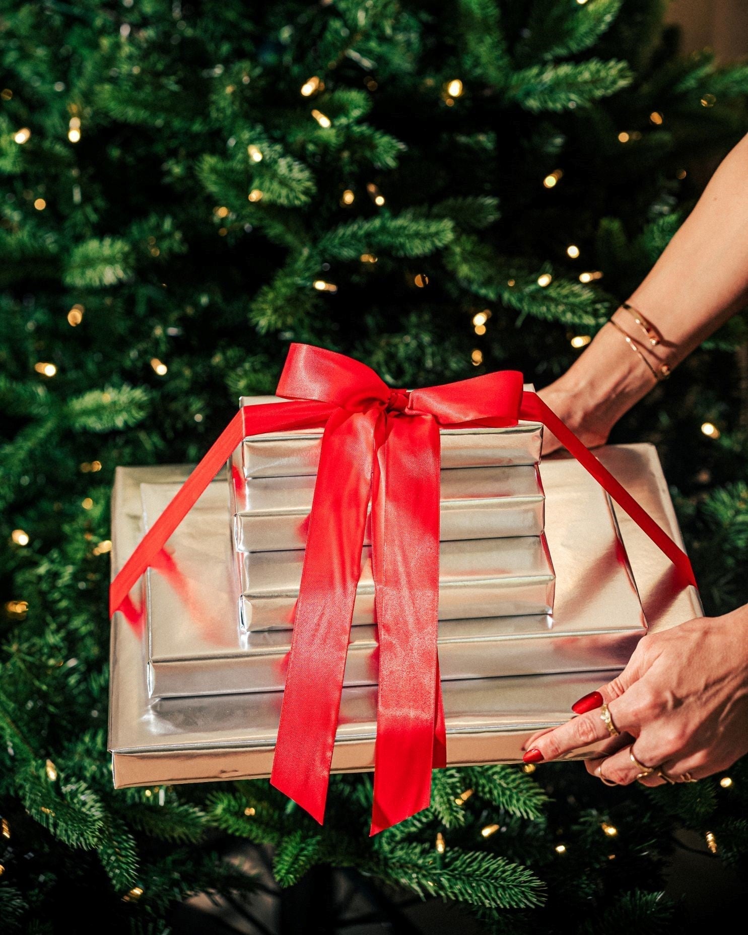 A woman holding gold-wrapped gifts in front of a Christmas tree.