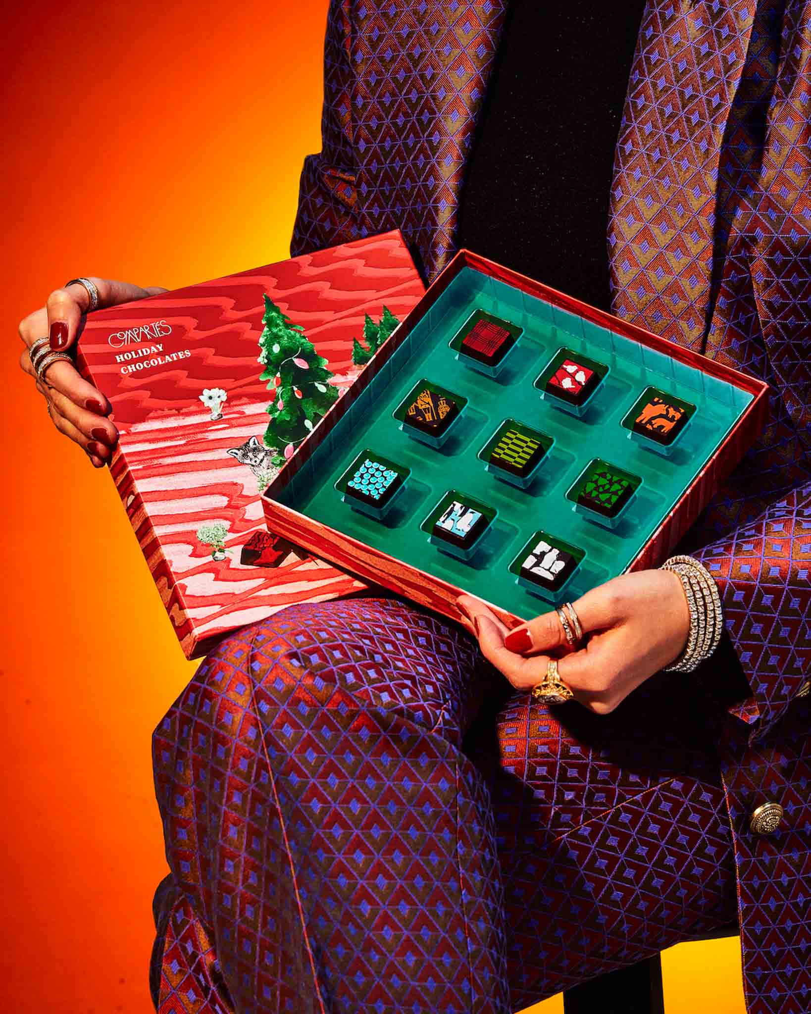 Person in a purple patterned suit, holding open the Compartés' chocolate Christmas candy gift box