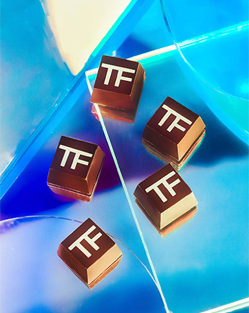 Tom Ford branded square chocolates by Compartés on a blue and pruple, glass-like surface.