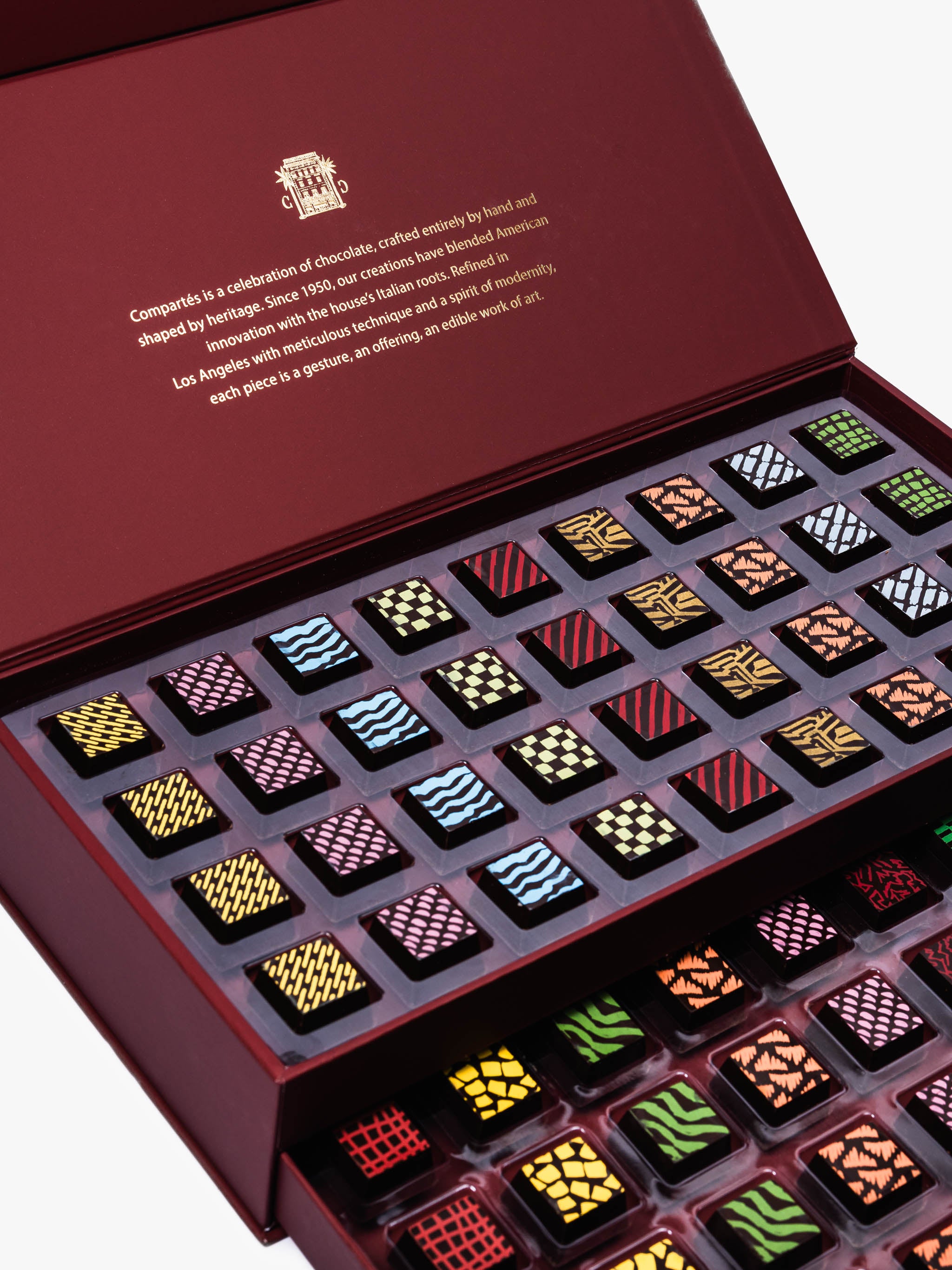 Compartes Burgundy Signature Drawer Collection featuring 80 handcrafted chocolates in a burgundy box with gold foil and geometric designs.