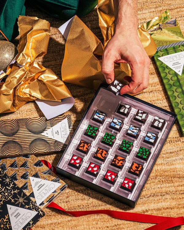 Christmas Chocolates being unwrapped and opened on a floor with Compartes Chocolate bars beside the box