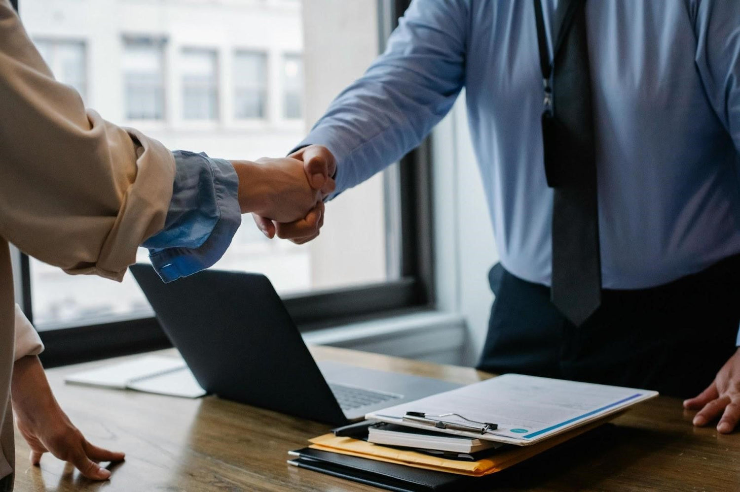 Two colleagues exchange a handshake in a corporate setting.