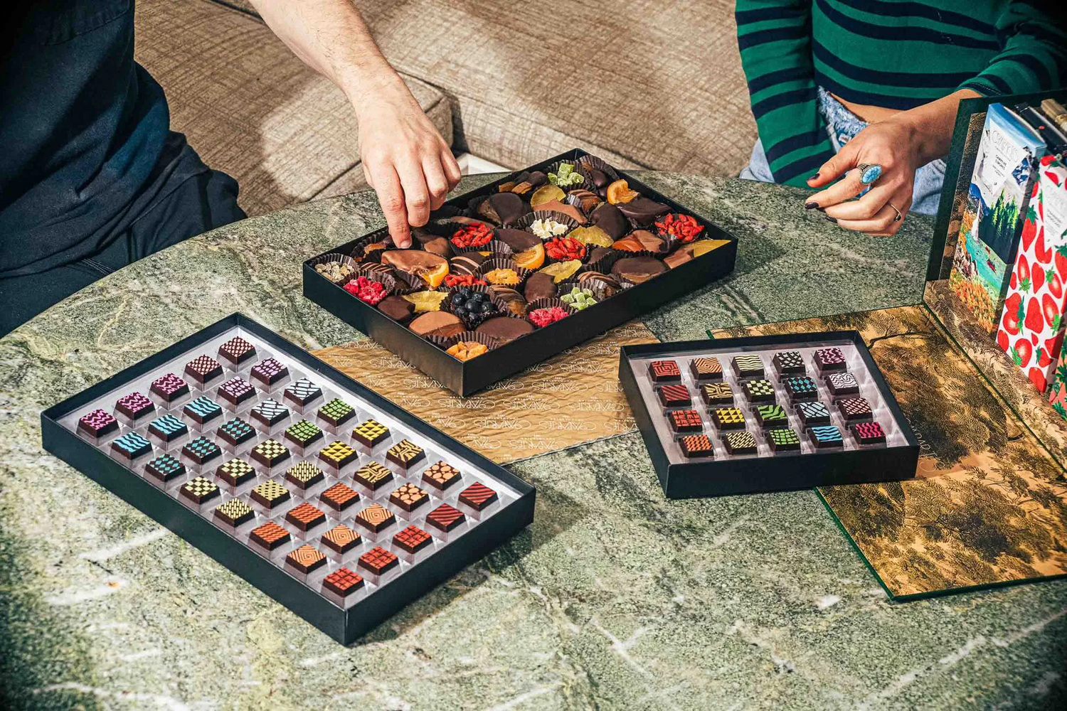 Two people selecting truffles and fruit from various Compartés selection boxes.