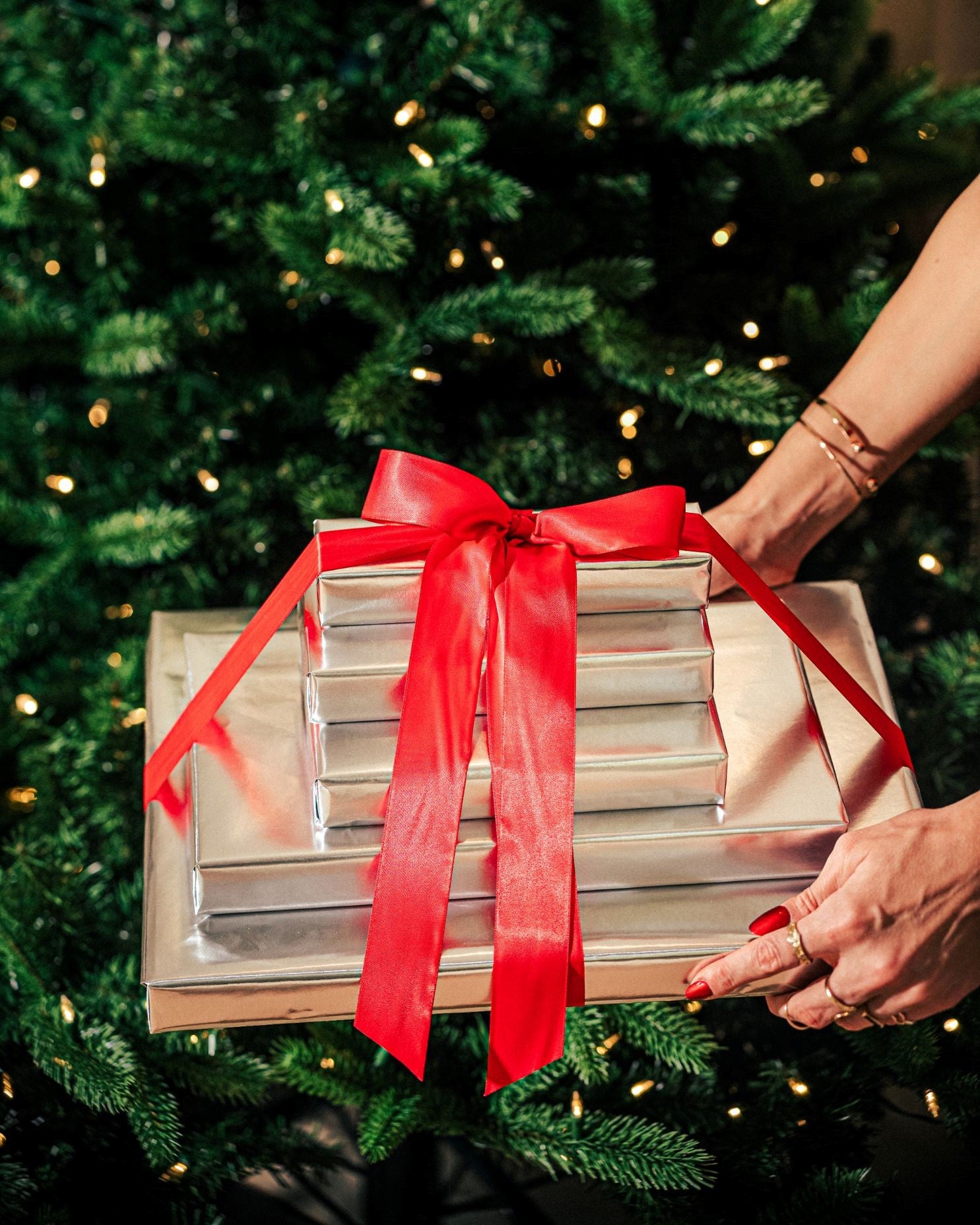 A woman holding out gifts in front of a Christmas tree  – Compartés