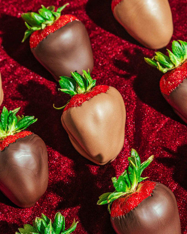 Variety of milk and dark chocolate dipped strawberries laid out on red sequin background