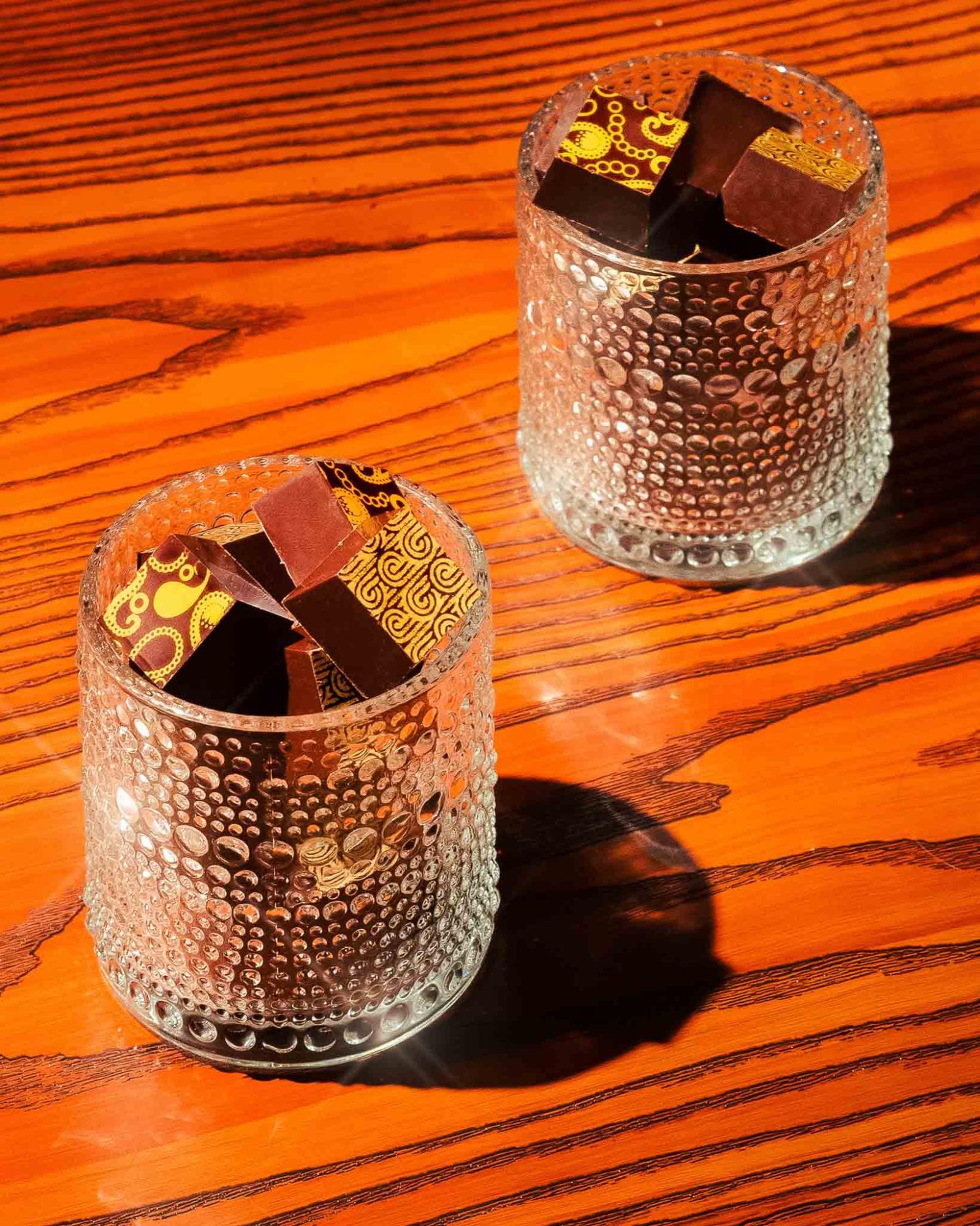 Dark chocolate truffles in textured whisky glasses on a wood tabletop.