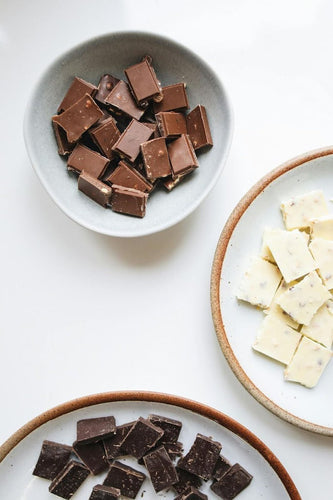 An assortment of white, dark, and milk chocolate pieces on white dishes – Compartés