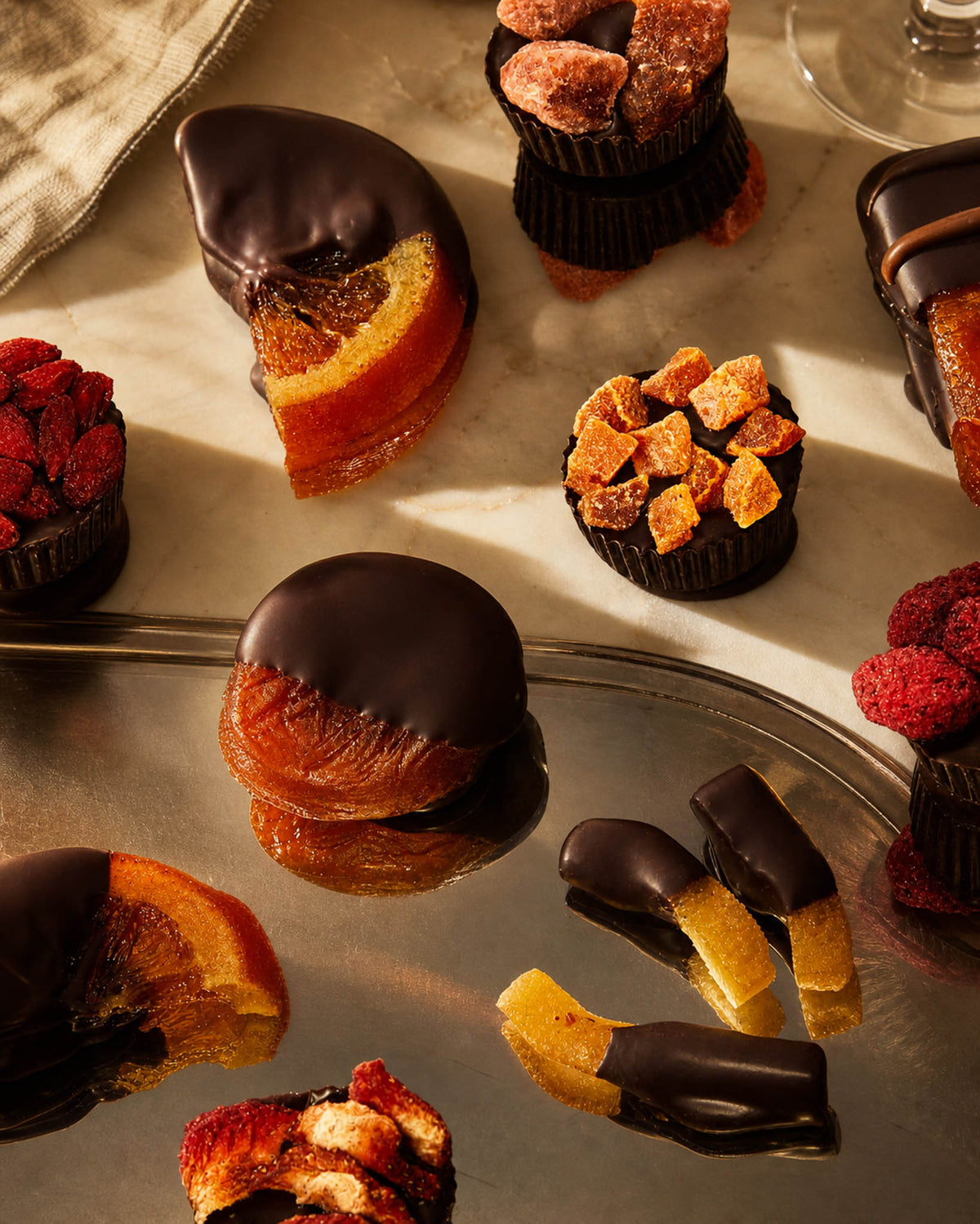 An assortment of gourmet chocolate-dipped fruits including dark chocolate-covered orange slices, raspberries, and apricots. Handmade artisan chocolate covered fruits by Compartes Los Angeles.