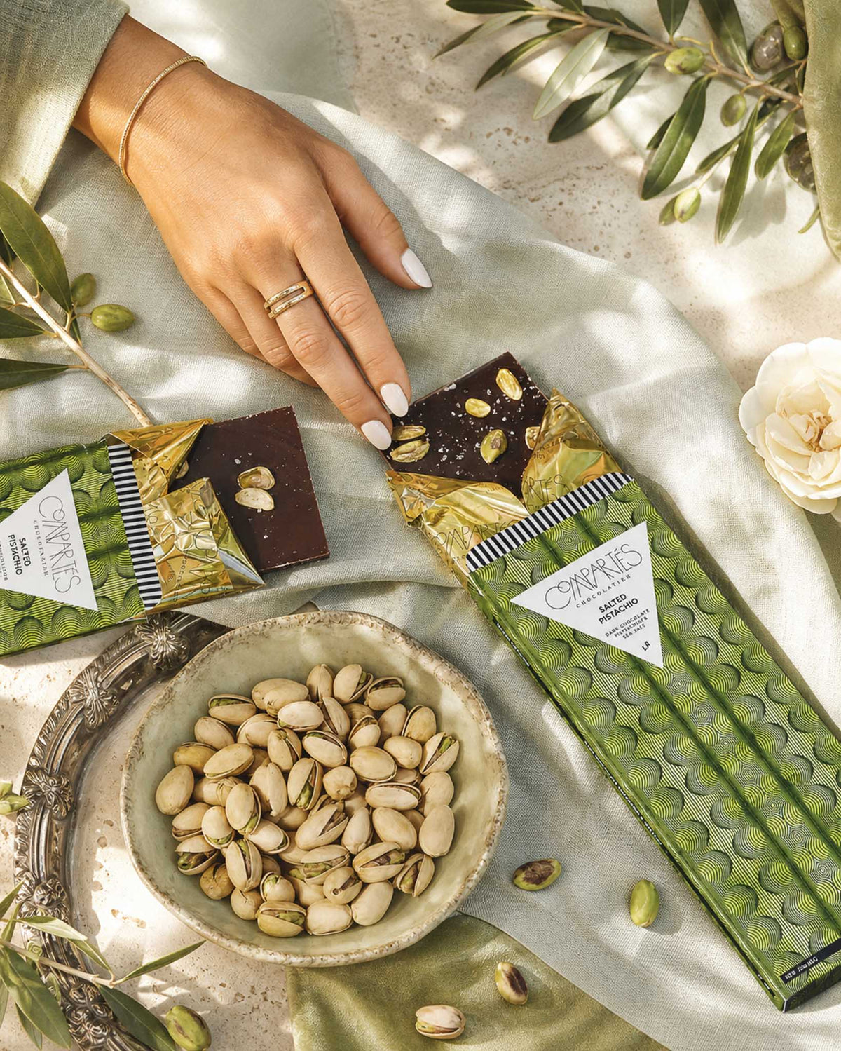A gourmet vegan Compartes chocolate bar package and a broken piece of dark chocolate with pistachios handmade in Los Angeles. 