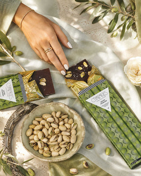 A gourmet vegan Compartes chocolate bar package and a broken piece of dark chocolate with pistachios handmade in Los Angeles. 