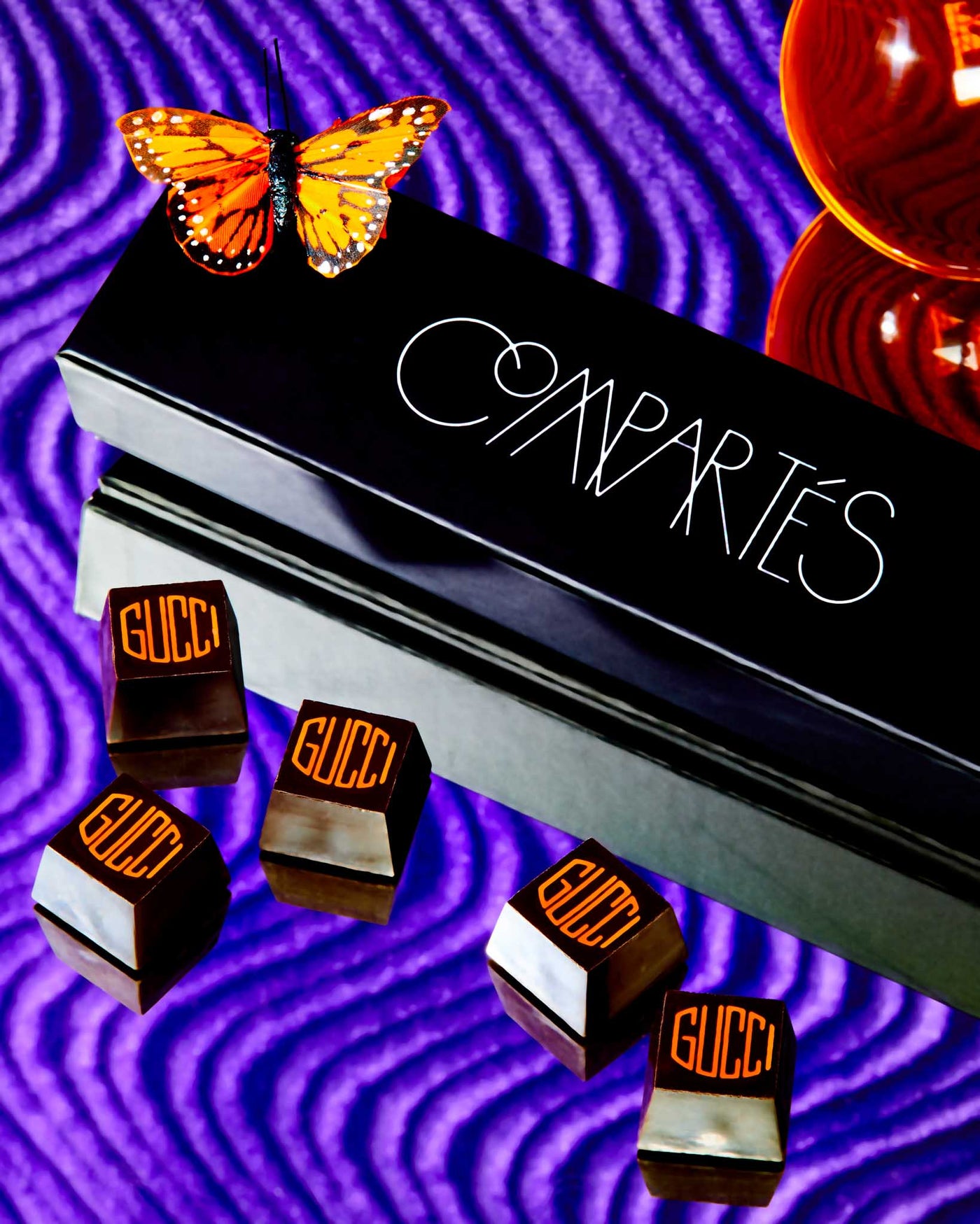 Compartes branded chocolates on top of a purple background, with a butterfly on top	