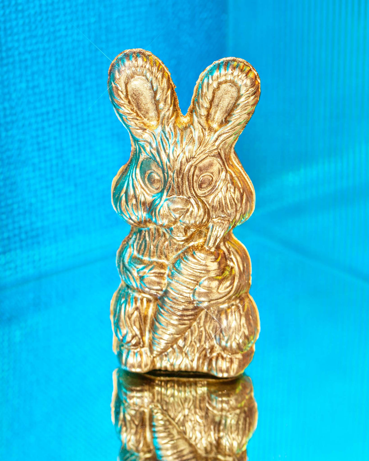 Gold chocolate bunny in front of a blue background	